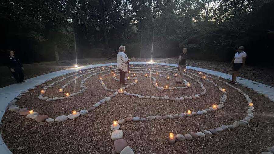The labyrinth at dusk, a tealight set beside every stone, four people walking the path