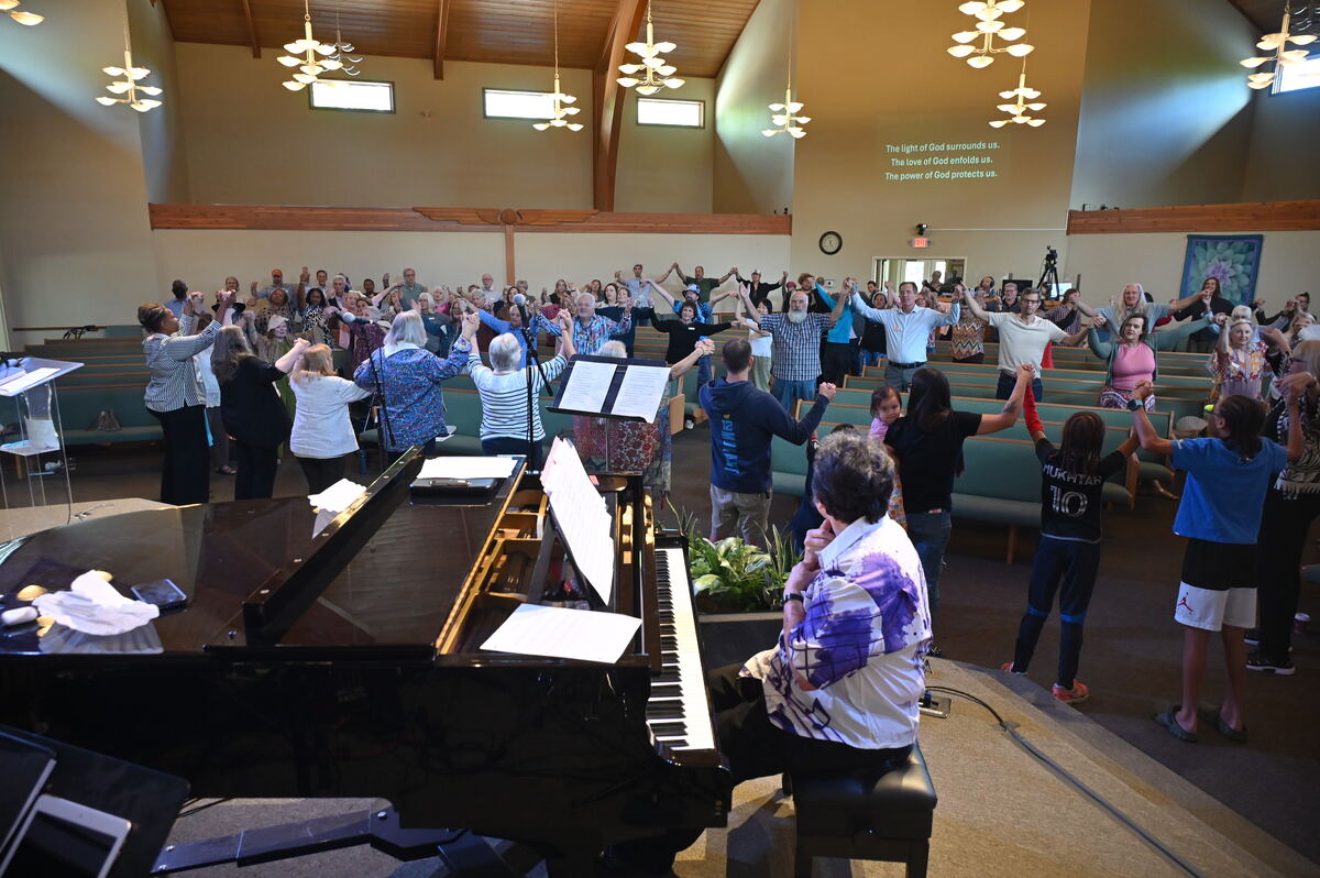The whole congregation standing with arms raised, seen from the front of the sanctuary