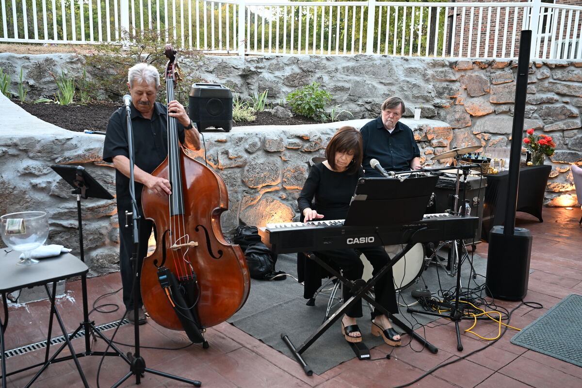 Two musicians on the patio in the late afternoon, an upright bass player standing and a keyboard player seated
