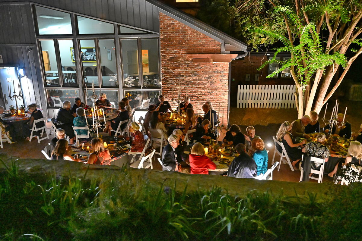 Guests seated at candlelit tables under the eaves of the building, seen from the lawn below