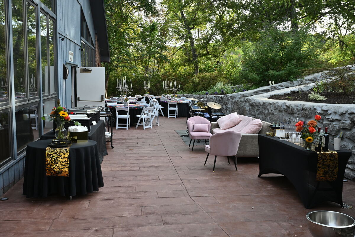 The patio set for the Gala before guests arrived — black-draped tables, lounge chairs and the stone wall beyond