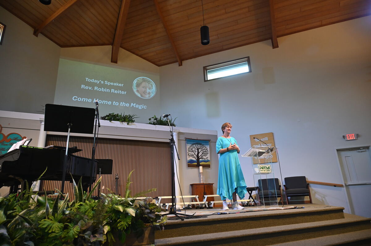Rev. Robin Reiter on the platform, the screen behind her reading Today's Speaker, Rev. Robin Reiter — Come Home to the Magic