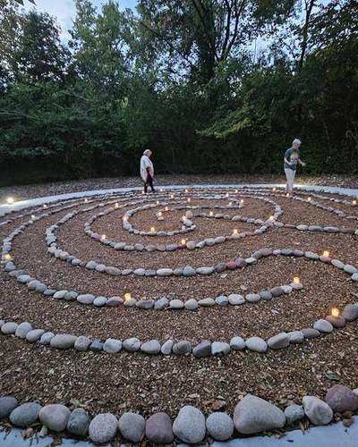 The full stone labyrinth at dusk, candles along every ring, two people walking