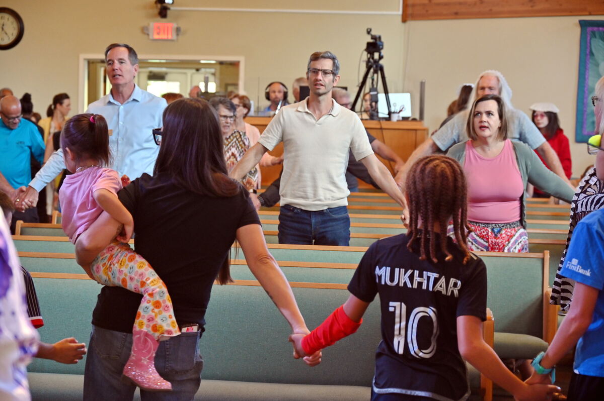 The congregation standing and holding hands in a circle across the sanctuary, families and children among them